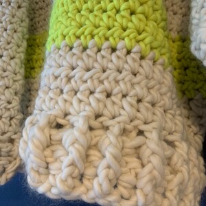 May include: A chunky hand-crocheted garment featuring thick, textured yarn in alternating horizontal stripes of off-white and vibrant neon yellow. The stitch pattern displays a dense, raised construction with visible loops and a soft, fuzzy fiber texture.