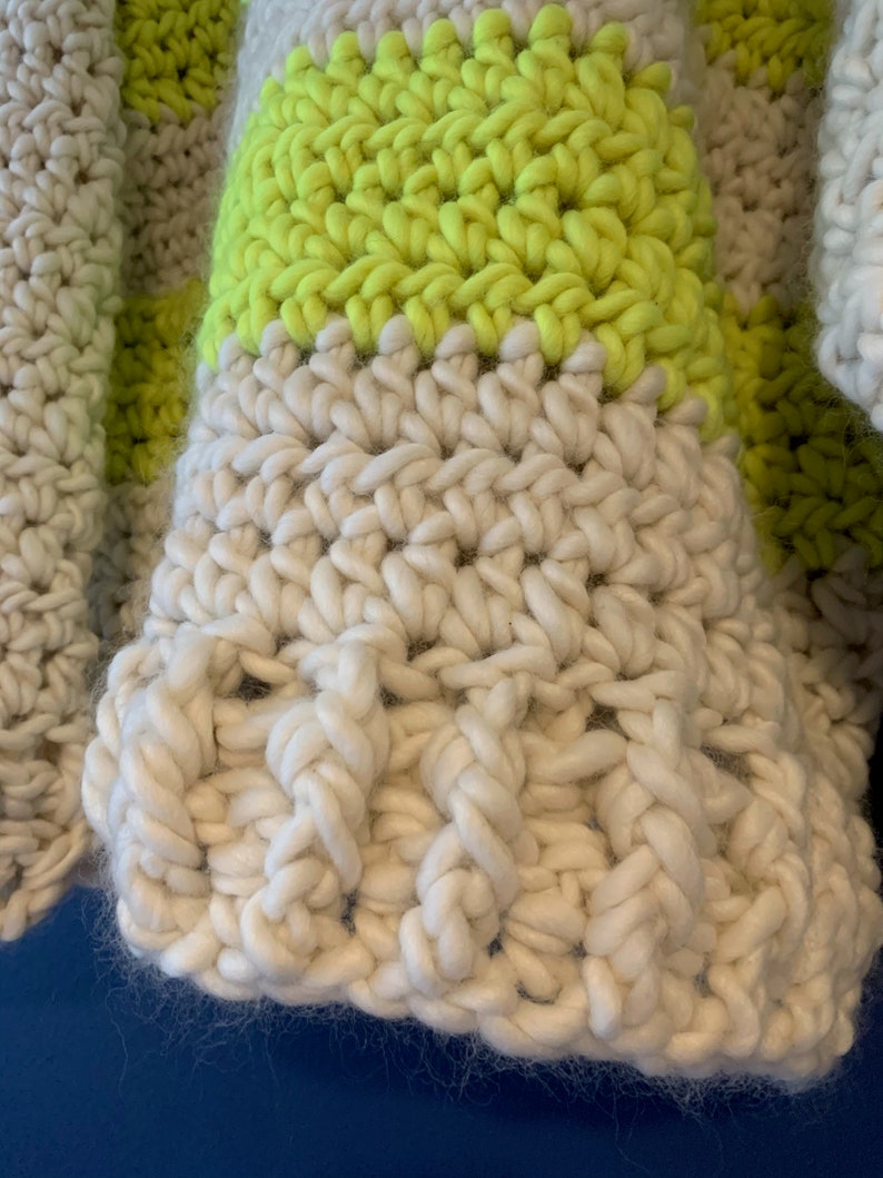 May include: A chunky hand-crocheted garment featuring thick, textured yarn in alternating horizontal stripes of off-white and vibrant neon yellow. The stitch pattern displays a dense, raised construction with visible loops and a soft, fuzzy fiber texture.