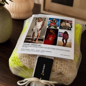 May include: A folded neon yellow and cream crochet textile packaged in clear plastic. A white informational card titled JULIE COLQUITT CROCHET, UNRAVELLED is attached, featuring five photographs of crochet garments and a black branded hang tag tied with string.