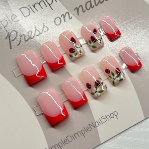 May include: A set of press-on nails with a red French tip design and ladybug and floral accents. The nails are displayed on a white card with the text "Simple Dimple Nail Shop Press on nails".