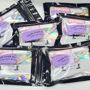 May include: Several clear plastic bags containing nail starter kits. Each kit includes a purple nail file, a pink and white nail glue tube, a wooden cuticle pusher, and a gray nail file. The text "Simple Dimple Nail Shop" and "Starter Kit" are visible.