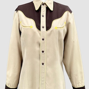 May include: A long-sleeve button-down shirt featuring a tan body with dark brown yokes and cuffs. The shirt includes yellow piping accents along the yokes and pockets, a pointed collar, and dark brown buttons down the front placket.