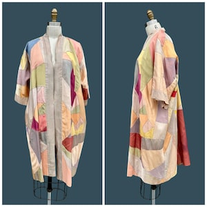 May include: A patchwork kimono-style jacket in pastel shades of pink, yellow, and blue. The jacket is displayed on a mannequin, showing its open front and three-quarter sleeves. The design features geometric shapes and is made of fabric.