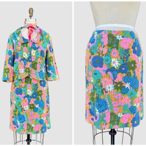 May include: A vintage floral print skirt suit. The set includes a jacket with a rounded collar and a matching knee-length skirt. The fabric features a vibrant pattern of pink, blue, green, and white flowers. The jacket has three-quarter sleeves.
