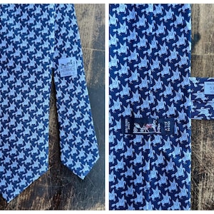 Può includere: Una cravatta in seta blu navy con un motivo ripetuto di cavalli alati azzurri. Include un'etichetta con la scritta HERMES PARIS, un'etichetta con MADE IN FRANCE 5117 HA 100% SOIE e un'etichetta nera con l'icona di una carrozza e 100% SILK.