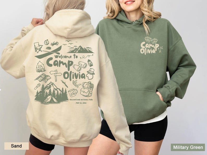 May include: A sand-colored hoodie with a dark green graphic on the back featuring camping icons, mountains, and the text Welcome to Camp Olivia Yellowstone National Park May 11, 2022. A military green hoodie with a small matching logo on the front.