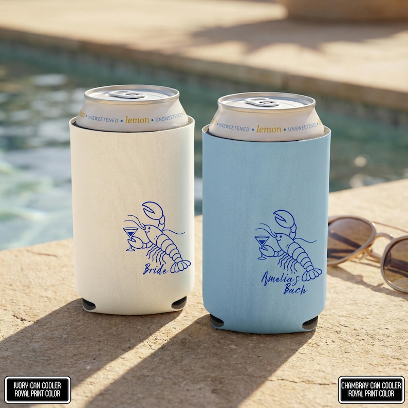 May include: Two cylindrical foam can coolers, one ivory and one chambray blue, each holding a lemon-flavored beverage can. Both feature a royal blue graphic of a lobster holding a martini glass, with the text Bride on one and Amelia's Bach on the other.