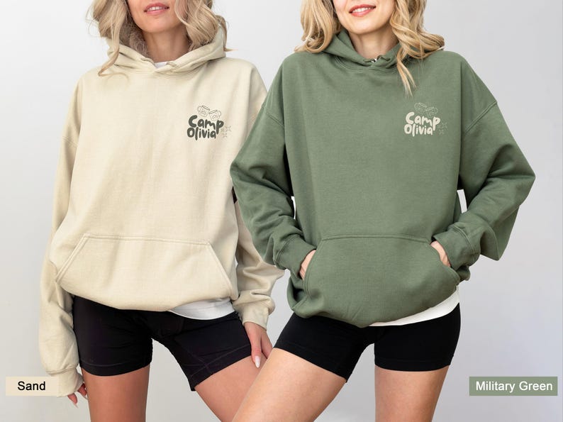 Puede incluir: Dos sudaderas con capucha en colores arena y verde militar. Cada una cuenta con un bolsillo tipo canguro frontal y un peque&ntilde;o gr&aacute;fico en el pecho izquierdo con el texto Camp Olivia junto a una estrella peque&ntilde;a y unos binoculares.