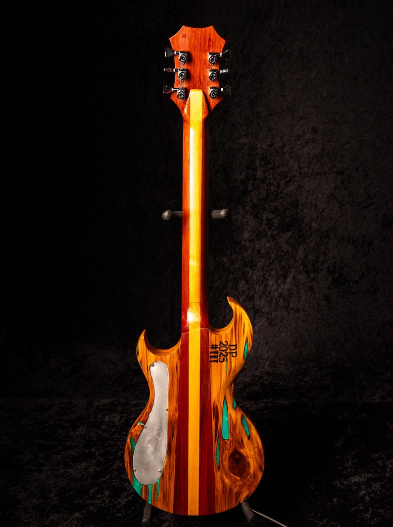 May include: A custom electric guitar with a unique wood grain pattern. The body features a mix of red, orange, and yellow wood, with a silver pickguard and turquoise accents. The headstock and neck are a rich brown.