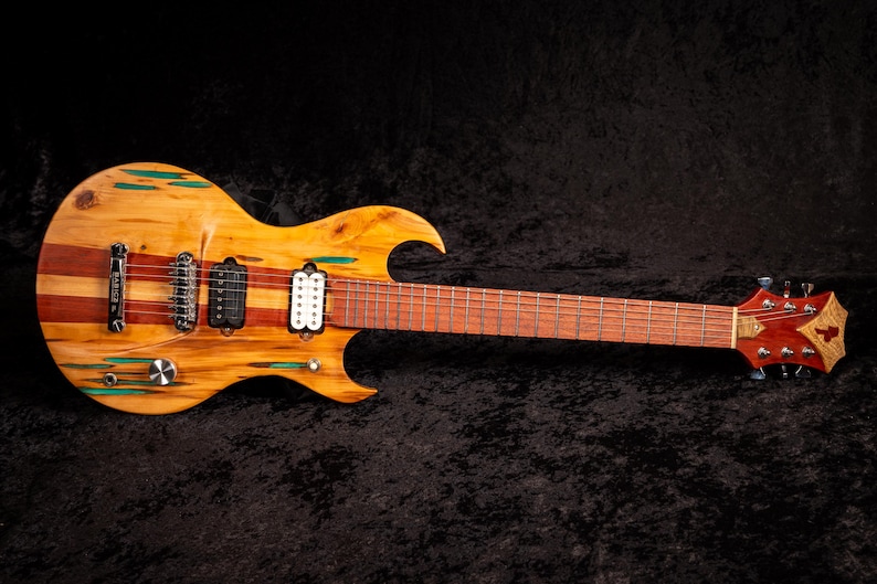 May include: A custom electric guitar with a unique design. The body features a combination of light and dark wood, with green accents. The neck and headstock are a darker wood, and the guitar has multiple pickups and tuning pegs.
