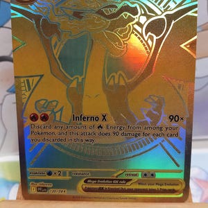 Puede incluir: Carta coleccionable Pokémon Mega Charizard X EX holográfica. La tarjeta presenta un fondo dorado con una ilustración detallada de Charizard. El texto incluye "Inferno X" y "HP 360".