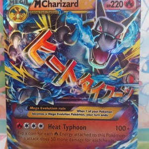 Könnte beinhalten: Eine Pokémon-Karte von Mega MCharizard EX mit einer dynamischen Illustration eines feurigen Drachen und japanischem Text. Die Karte hat 220 HP und enthält Angriffsdetails. Sie enthält eine Pokémon EX-Regel, auf blau-orangefarbenem Hintergrund.