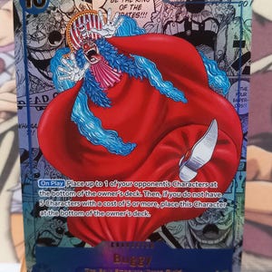 Puede incluir: Carta coleccionable con el personaje Buggy de la serie One Piece. La carta muestra a Buggy en una pose dinámica con una capa roja y pelo azul, con el texto "I WANNA BE THE KING OF THE PIRATES!!!".