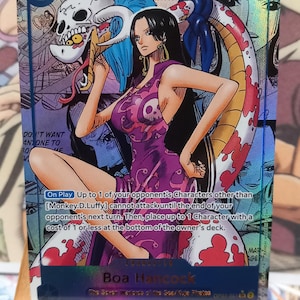Può includere: Carta collezionabile di One Piece con Boa Hancock. La carta mostra un'illustrazione colorata del personaggio in un vestito viola, con il testo « BECAUSE I'M BEAUTIFUL ». La carta ha una speciale finitura olografica.