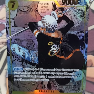 以下が含まれることがあります： アニメ「ワンピース」に登場するトラファルガー・ローのホログラフィックトレーディングカード。カードにはキャラクターイラスト、テキスト、パワーレベル9000が記載されています。カードの背景は、カラフルなマンガ風イラストです。