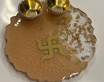 May include: A decorative resin tray with two gold-coloured bowls. The tray features a peach-coloured base with a gold-coloured Swastika symbol and gold leaf accents. The bowls have a decorative beaded edge.