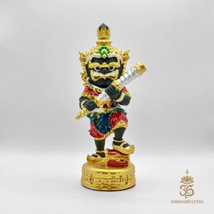 Può includere: Statuetta dettagliata di una divinità, con volto nero, dettagli dorati, corona gioiello e abiti ornati in rosso, verde e blu. La figura tiene in mano un bastone d'argento e oro e si erge su una base dorata.