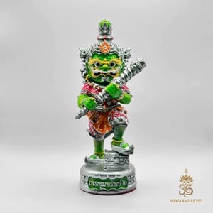 Può includere: Statuetta verde e argento di un Yaksha thailandese, un gigante mitico. La figura indossa una corona, abiti ornati e tiene in mano un'arma. La base ha un testo in scrittura thailandese. Su sfondo bianco.