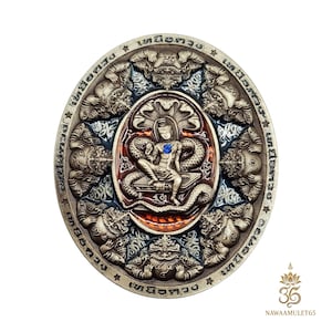 Puede incluir: Un amuleto circular plateado con intrincados grabados en relieve. El diseño central presenta una figura sentada con una gema azul, rodeada por una serpiente y otras criaturas míticas. El anillo exterior tiene figuras y texto adicionales.