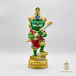Può includere: Statuetta dettagliata di una divinità verde e oro, con in mano un bastone bianco e oro. La figura indossa un abito rosso e oro e una corona d'oro con accenti blu. La base è dorata con testo inciso.