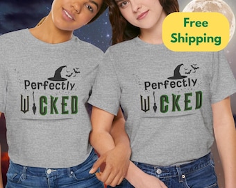 May include: Two women wearing gray t-shirts with the words "Perfectly Wicked" printed on the front. The design includes a witch hat, bats, and a green and black color scheme. The shirts are paired with blue jeans.