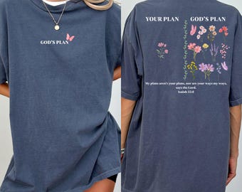 May include: A dark blue t-shirt with the text "GOD'S PLAN" and a butterfly graphic on the front. The back of the shirt features the text "YOUR PLAN GOD'S PLAN" with floral illustrations and the quote "My plans aren't your plans, nor are your ways my ways, says the Lord. Isaiah 55:8."