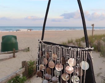 May include: A black handbag featuring a single strap and a decorative front panel adorned with vertical strands of clear beads interspersed with circular, iridescent mother-of-pearl discs that hang freely from the top edge of the bag.