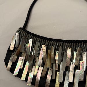 May include: Black satin handbag with a beaded top and a black handle. The bag is adorned with rectangular iridescent shell pieces that hang down from the top of the bag.