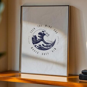 May include: A framed print with a navy blue wave design and the words "EVEN THE WIND AND WAVES OBEY HIM" arranged in a circle. The print is displayed on a wooden shelf, with books stacked nearby.