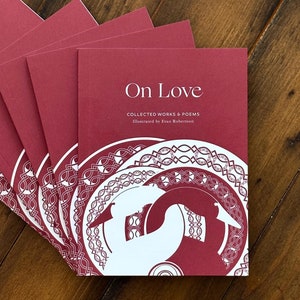 May include: A stack of burgundy-colored books with the title "On Love: Collected Works & Poems" illustrated by Evan Robertson. The cover features a white illustration of a stylized bird with a decorative pattern.