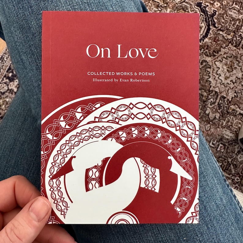 May include: A red book titled "On Love: Collected Works & Poems" illustrated by Evan Robertson. The cover features a white illustration of a stylized bird with a Celtic knot design.