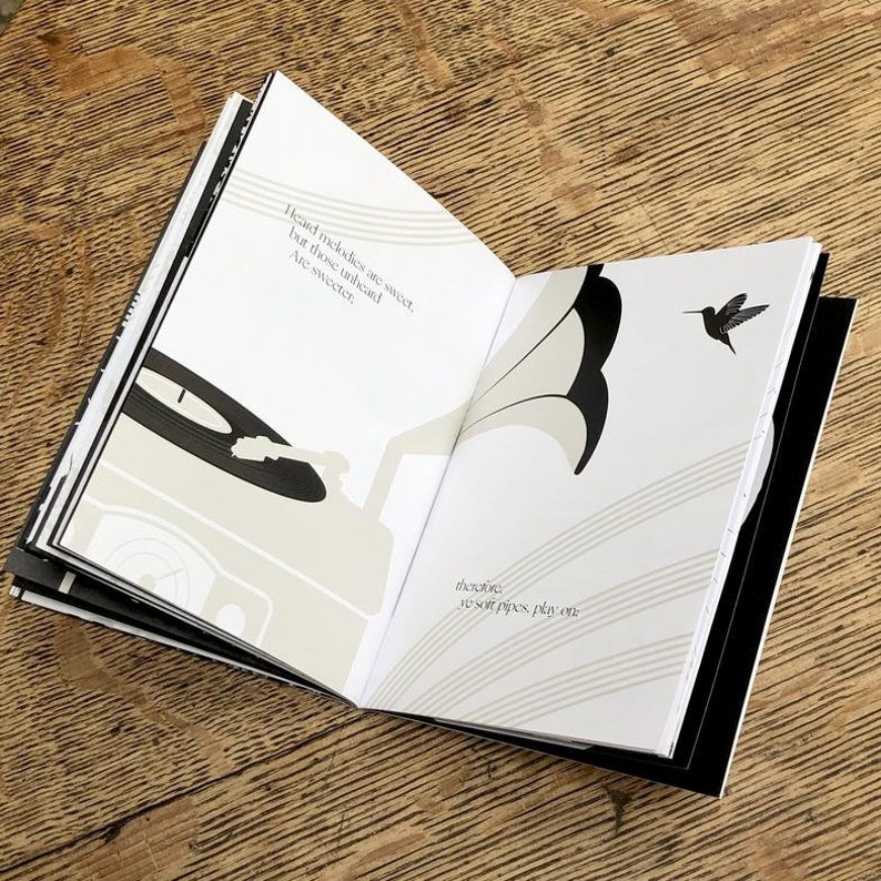 K&ouml;nnte beinhalten: Ein offenes Buch mit Schwarzwei&szlig;illustrationen eines Plattenspielers und eines Kolibris. Der Text auf der Seite lautet "Heard melodies are sweet, but those unheard are sweeter. Thereof, as soft pipes play on."