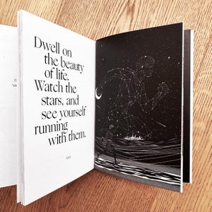 Op de afbeelding: Een open boek met een zwart-witte illustratie van een persoon die onder een sterrenhemel rent. De tekst op de linkerpagina luidt: "Dwell on the beauty of life. Watch the stars, and see yourself running with them."
