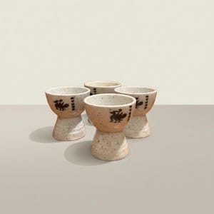 May include: A set of three ceramic nesting bowls in graduating sizes. The bowls feature a speckled, matte finish in shades of cream, light brown, and dark brown. The largest bowl measures approximately 8 inches in diameter.