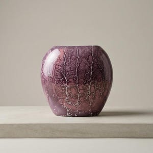 May include: A decorative, round vase with a textured, crackled pattern in shades of purple and pink. The vase has a glossy finish and sits on a neutral-colored surface, showcasing its unique design.