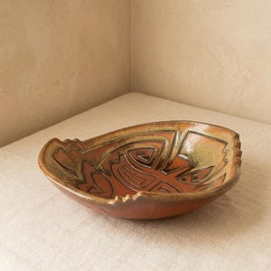 May include: A handcrafted ceramic bowl with a unique, geometric design. The bowl features a warm, earthy color palette with shades of brown, orange, and tan. The interior is a rich orange, while the exterior has a textured, matte finish.