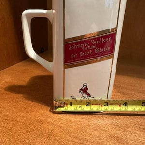 May include: A white ceramic pitcher with a rectangular shape and a handle. The pitcher features the "Johnnie Walker Red Label Old Scotch Whisky" logo in red and gold. The pitcher is approximately 4 inches wide.