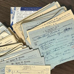 May include: A collection of vintage pharmacy documents, including prescription pads and invoices. The papers are aged with a mix of blue and cream colors, featuring handwritten notes and printed text. Some documents display the text "Bolivar, N.Y."