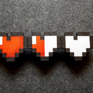 May include: Three pixelated hearts, one red, one half red and half white, and one white, against a dark gray background.