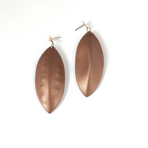 Könnte beinhalten: Ein Paar lange, braune, blattartige Ohrringe mit einer metallischen Oberfläche.