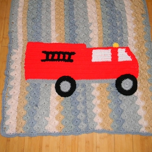 May include: A crocheted blanket featuring a repeating vertical wave pattern in shades of blue, beige, and white. Centered on the blanket is a large, bright red fire truck applique with black wheels, a black ladder, and white windows.