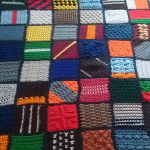 Könnte beinhalten: Eine handgefertigte Patchworkdecke mit einer Vielzahl von strukturierten Quadraten in einer Reihe von Farben, darunter Rot, Blau, Grün, Gelb und Orange. Die Decke ist aus Garn gefertigt und hat ein gemütliches, handwerkliches Aussehen.