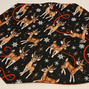 Peut inclure: Une jupe de sapin en tissu noir ornée d'un motif répétitif de cerfs bruns avec des bois, de flocons de neige blancs et d'étoiles dorées. Le design comprend des lignes rouges courbes serpentant entre les cerfs sur toute la surface.
