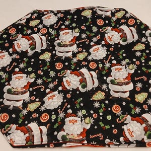 Peut inclure: Une jupe de sapin en tissu de forme hexagonale avec un fond noir orné d'un motif répétitif de personnages du Père Noël, de sucres d'orge, de tourbillons de menthe poivrée et de flocons de neige blancs sur des costumes rouges et blancs.
