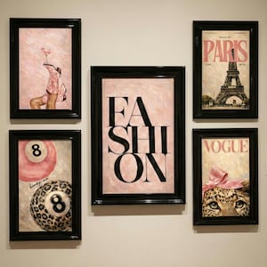 Op de afbeelding: Een verzameling ingelijste kunstwerken met zwarte lijsten. De kunstwerken omvatten een roze achtergrond met het woord "FASHION", een Vogue-magazinecover en een schilderij van een poolbal.