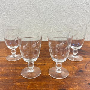 May include: A set of four clear glass goblets, each featuring a delicate etched wheat pattern on the bowl. The glasses have a short, rounded stem and a circular base, providing a stable foundation for each piece of clear, transparent glassware.