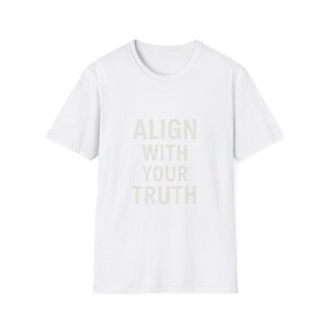 Può includere: Una maglietta bianca con la scritta "ALIGN WITH YOUR TRUTH" in grigio chiaro. La maglietta ha maniche corte e girocollo, adatta per un look casual.