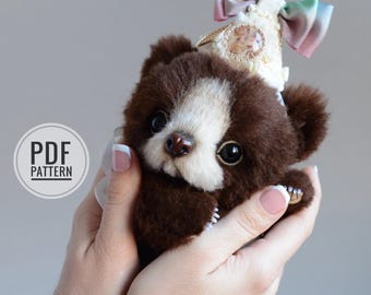 May include: A handmade brown and white teddy bear with a decorative bow. The bear has large, dark eyes and is held in someone's hands. The image includes the text "PDF PATTERN" in a circle.
