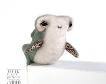 May include: A handmade plush shark toy with a light gray body, white belly, and patterned fins. The shark has large black eyes and a small smile. The text "PDF pattern + VIDEO" is visible in the lower left corner.