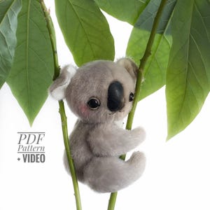 May include: A plush gray koala bear with a black nose and large, dark eyes, clinging to a green leafy branch. The koala has pink cheeks and white accents on its ears. The image includes the text "PDF Pattern + VIDEO".